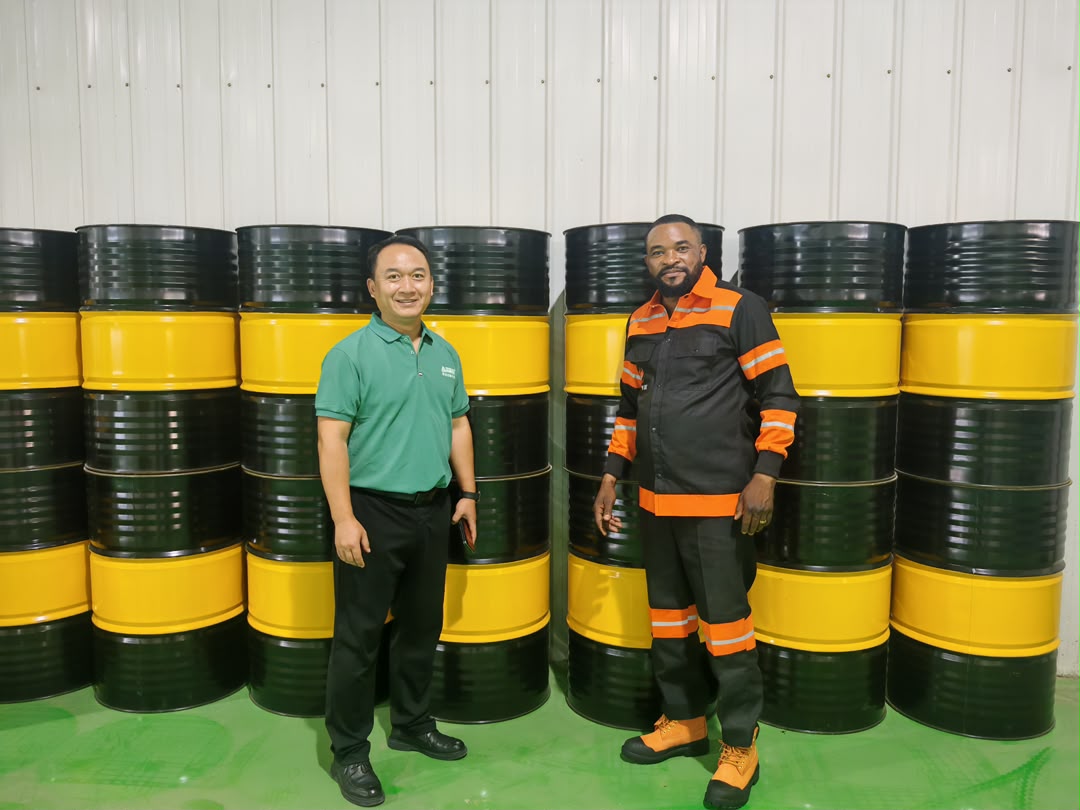 The founder with a partner in front of stacked lubricant drums